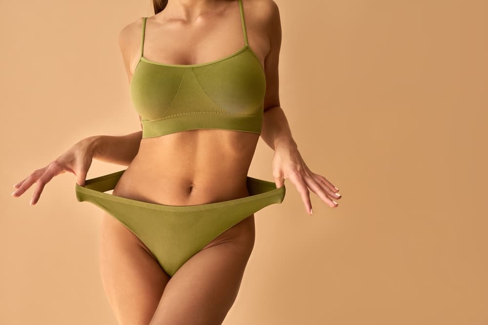 Close-up of a woman in green underwear gently pulling the waistband to show the bikini area, symbolising smooth results from a bikini wax.