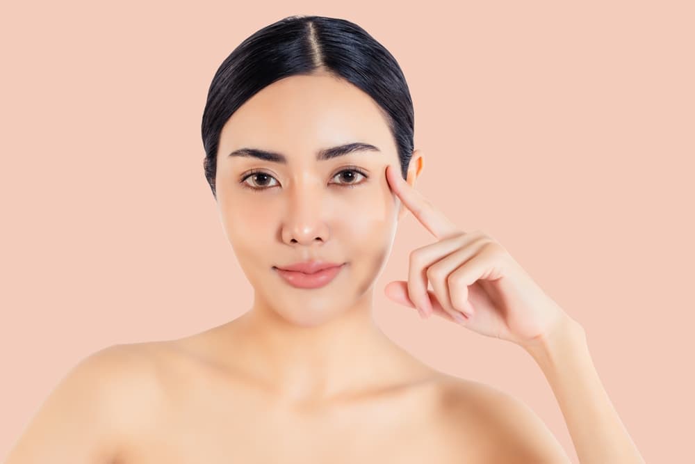Close-up of a woman with clear, smooth skin pointing to her chin area, representing hair-free results from chin threading or waxing.
