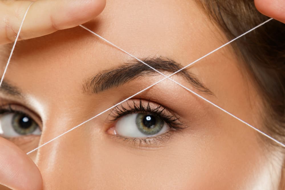 Close-up of a woman’s eyebrow being shaped with a threading technique, showing precise hair removal for perfectly defined brows.