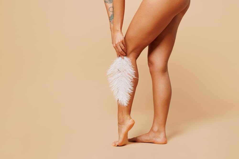 Close-up of smooth, hair-free legs holding a soft white feather, symbolising silky results from a full leg wax.