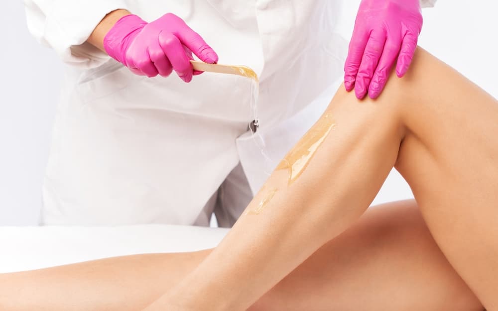 Beauty therapist applying warm wax to a client’s lower leg during a half leg waxing treatment for smooth, hair-free skin.