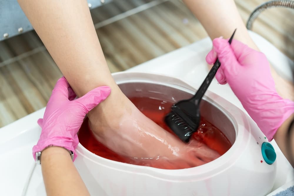 Therapist applying warm paraffin wax treatment to client’s feet during luxury pedicure at a salon.