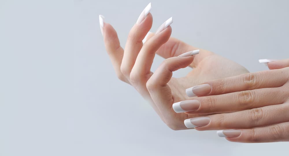 Close-up of hands with a flawless French gel manicure, showing glossy nude nails with crisp white tips.