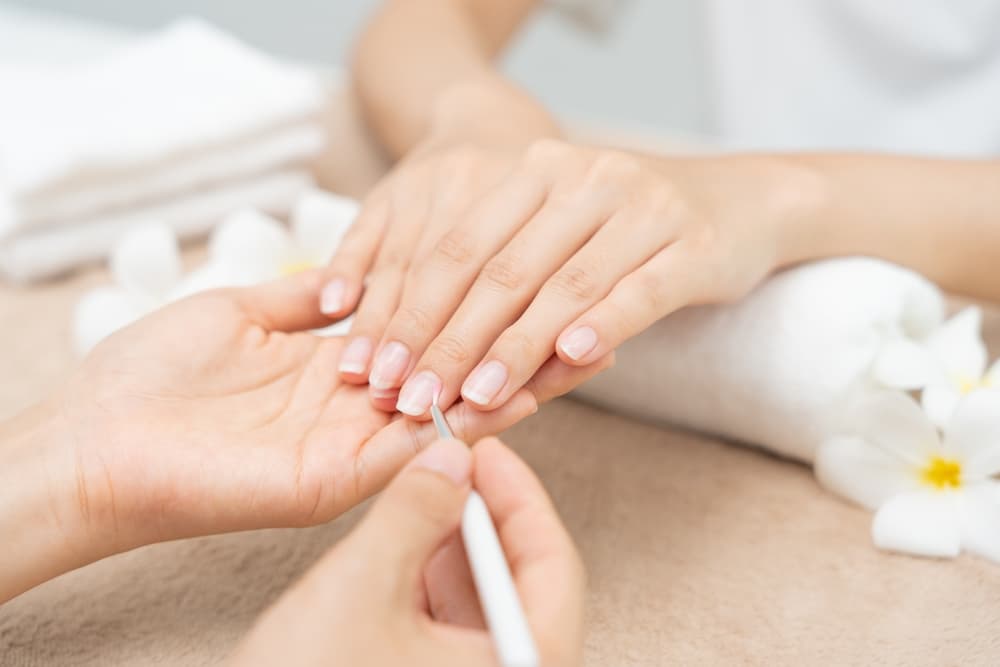 Close-up of a beauty therapist applying a nail protein treatment during a manicure, focusing on nail health and strength.